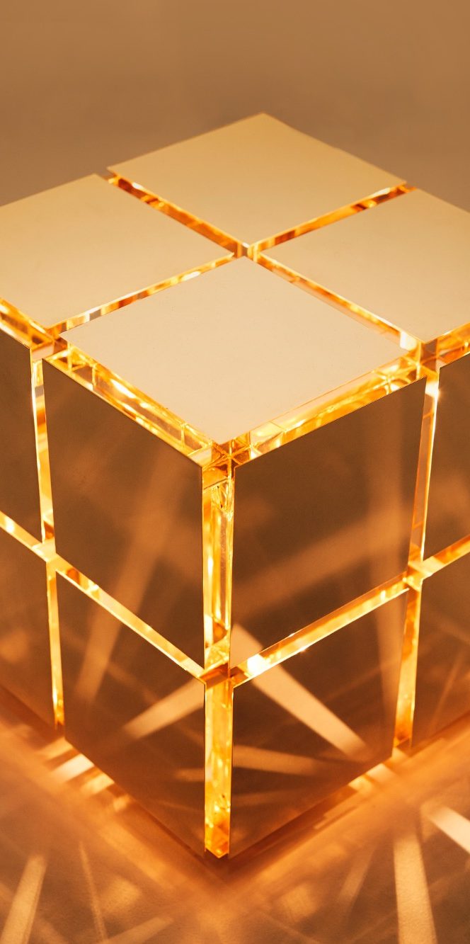 Cube de laiton poli avec des reflets dorés sur un fond neutre.