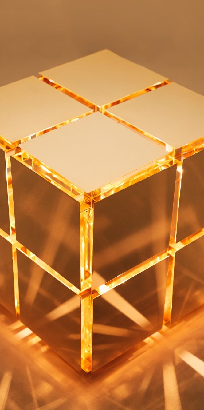 Cube de laiton poli avec des reflets dorés sur un fond neutre.