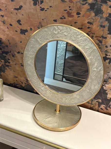 Miroir circulaire avec une base dorée, décoré d’un motif en relief.