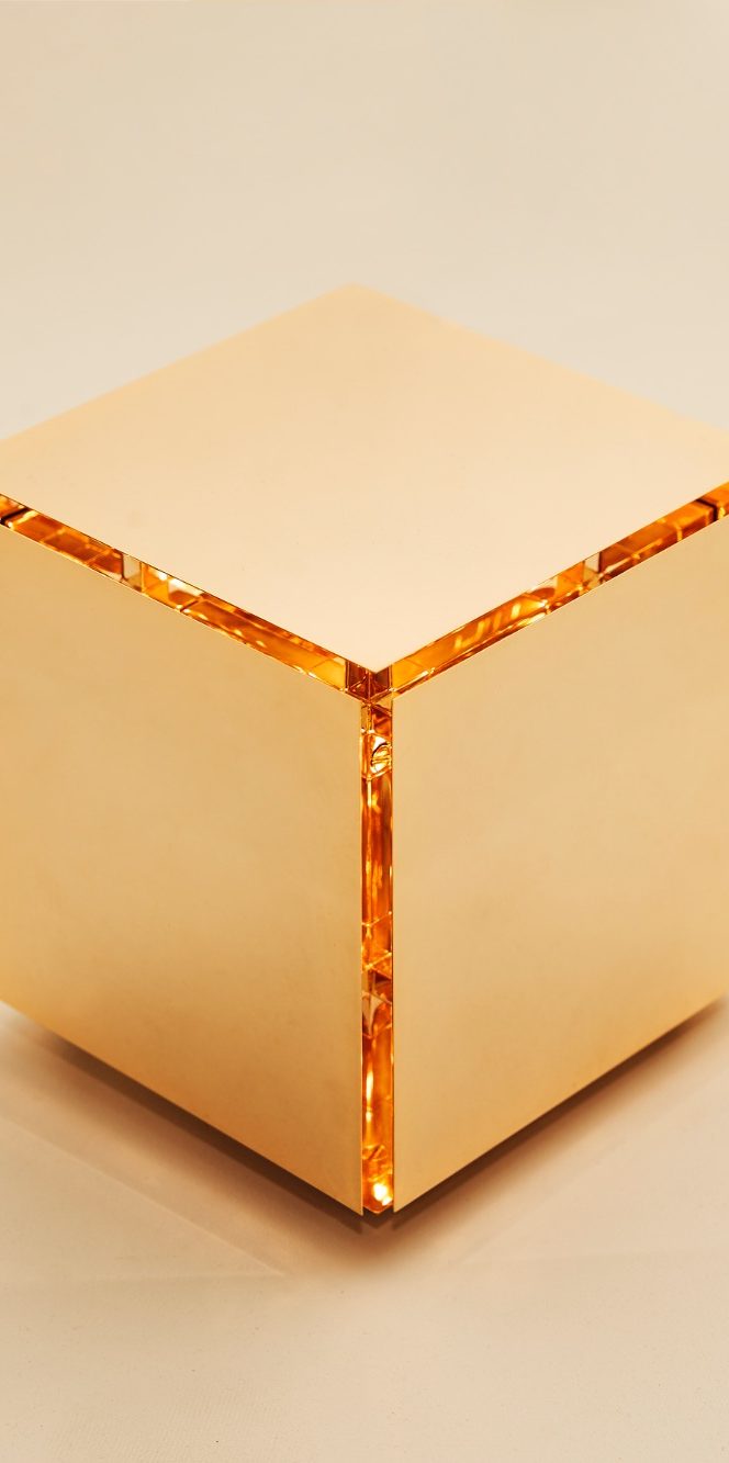 Cube doré brillant avec des bords lumineux, posé sur un fond neutre.