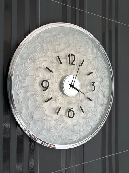 Horloge murale ronde avec cadran argenté et chiffres noirs, indiquant 9h12.