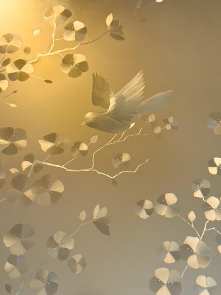 Oiseau stylisé sur une branche avec des feuilles délicates en arrière-plan.
