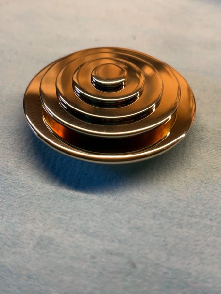 Bouton en métal poli en forme de spirale concentrique, avec des niveaux en relief.
