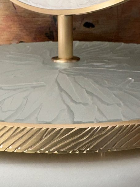 Base en métal doré avec un motif texturé et un support pour un objet dessus.