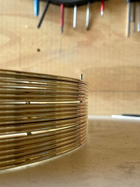 Bobine de fil métallique doré posée sur une surface, avec des outils en arrière-plan.