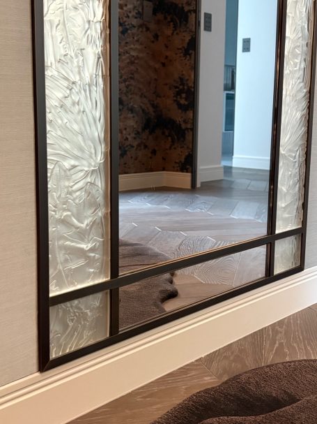 Un miroir avec un cadre en métal, reflétant un sol élégant et un mur texturé.