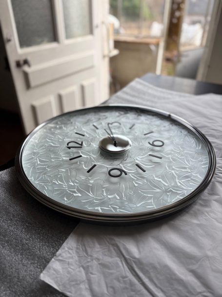 Horloge vintage en verre avec chiffres, posée sur une surface blanche.