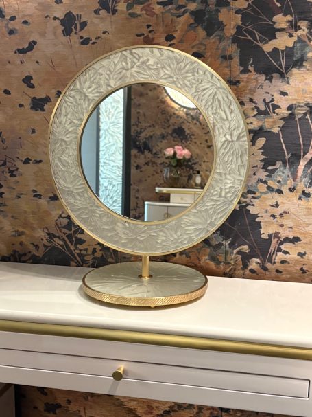 Miroir rond avec cadre doré décoré, posé sur une coiffeuse.